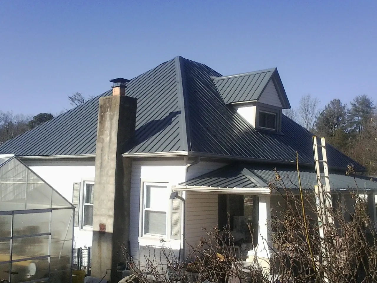 Dark blue standing seam metal roof on a white farmhouse with dormer — Slate & Tile Roof Repair by Roofing Brothers in Sweetwater