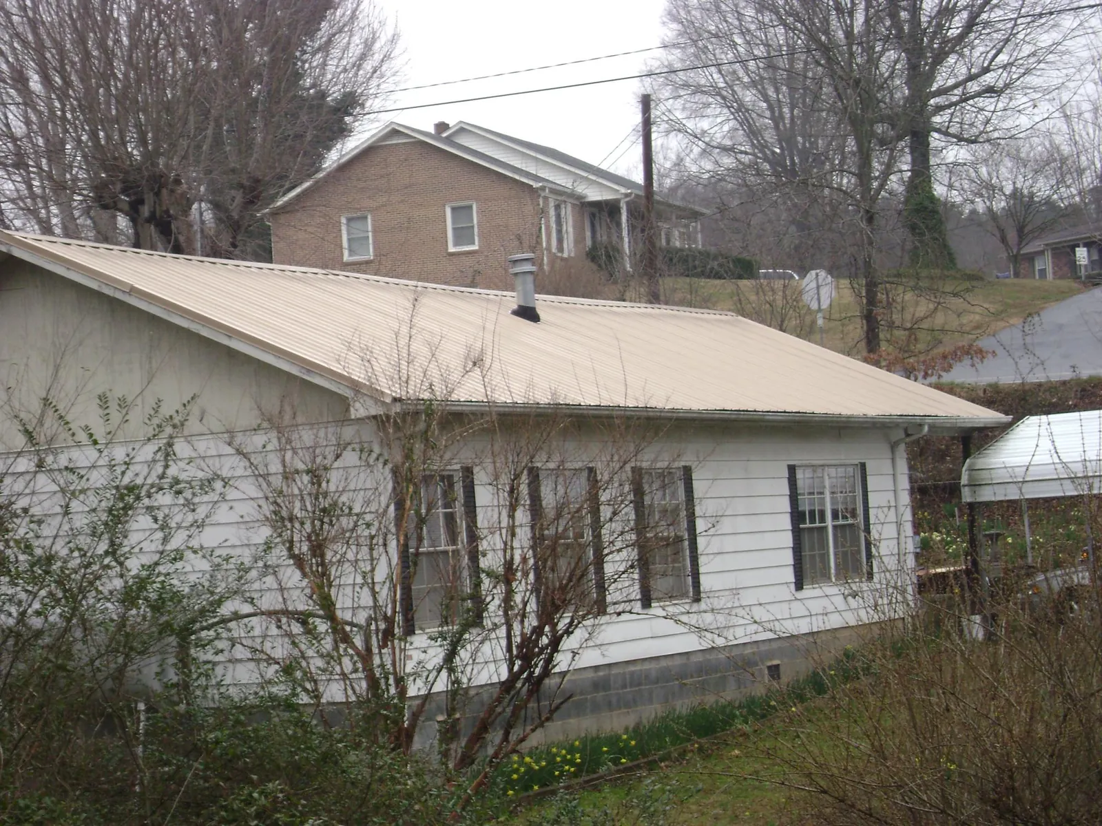 Tan metal roof on a white sided house set into a hillside — Commercial Roofing by Roofing Brothers in Sweetwater
